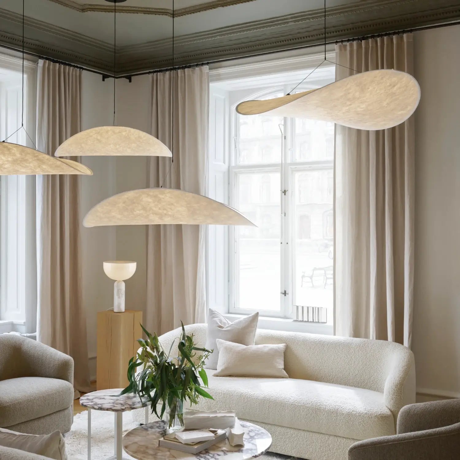 Bright and airy living room featuring a blend of contemporary and classic design elements. The space is anchored by a pair of off-white, textured sofas, accompanied by a marble-topped coffee table adorned with a simple bouquet of greenery.